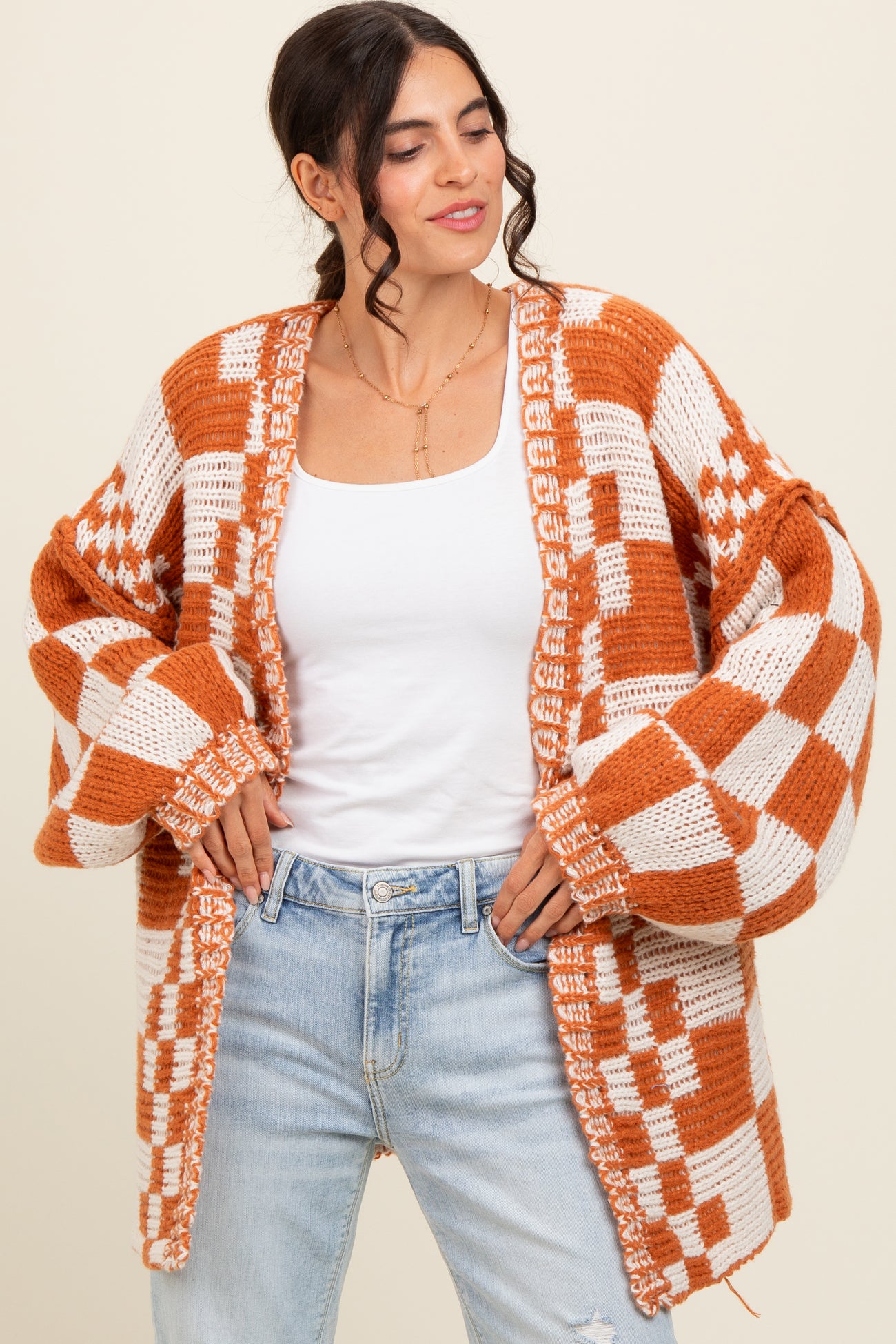 woman wearing an oversized orange and white checkered cardigan over a white tank top and distressed light wash jeans