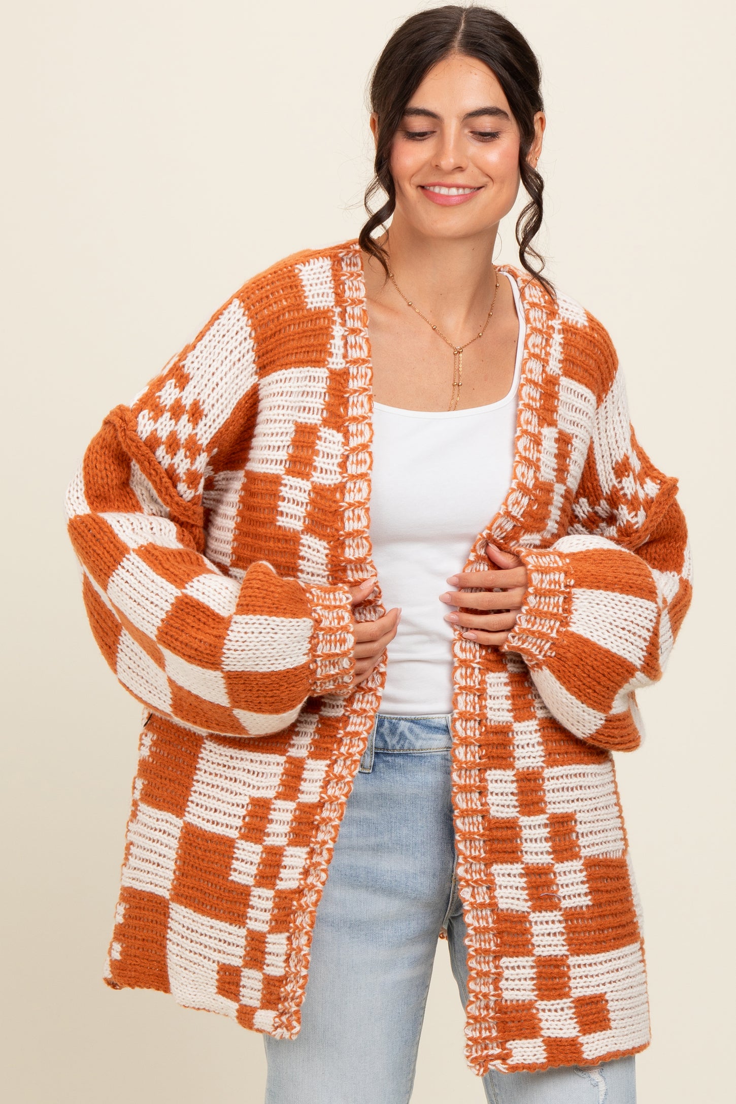 woman wearing an oversized orange and white checkered open knit cardigan over a white top and light blue jeans