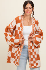 woman wearing an oversized orange and white checkered open knit cardigan over a white top and light blue jeans