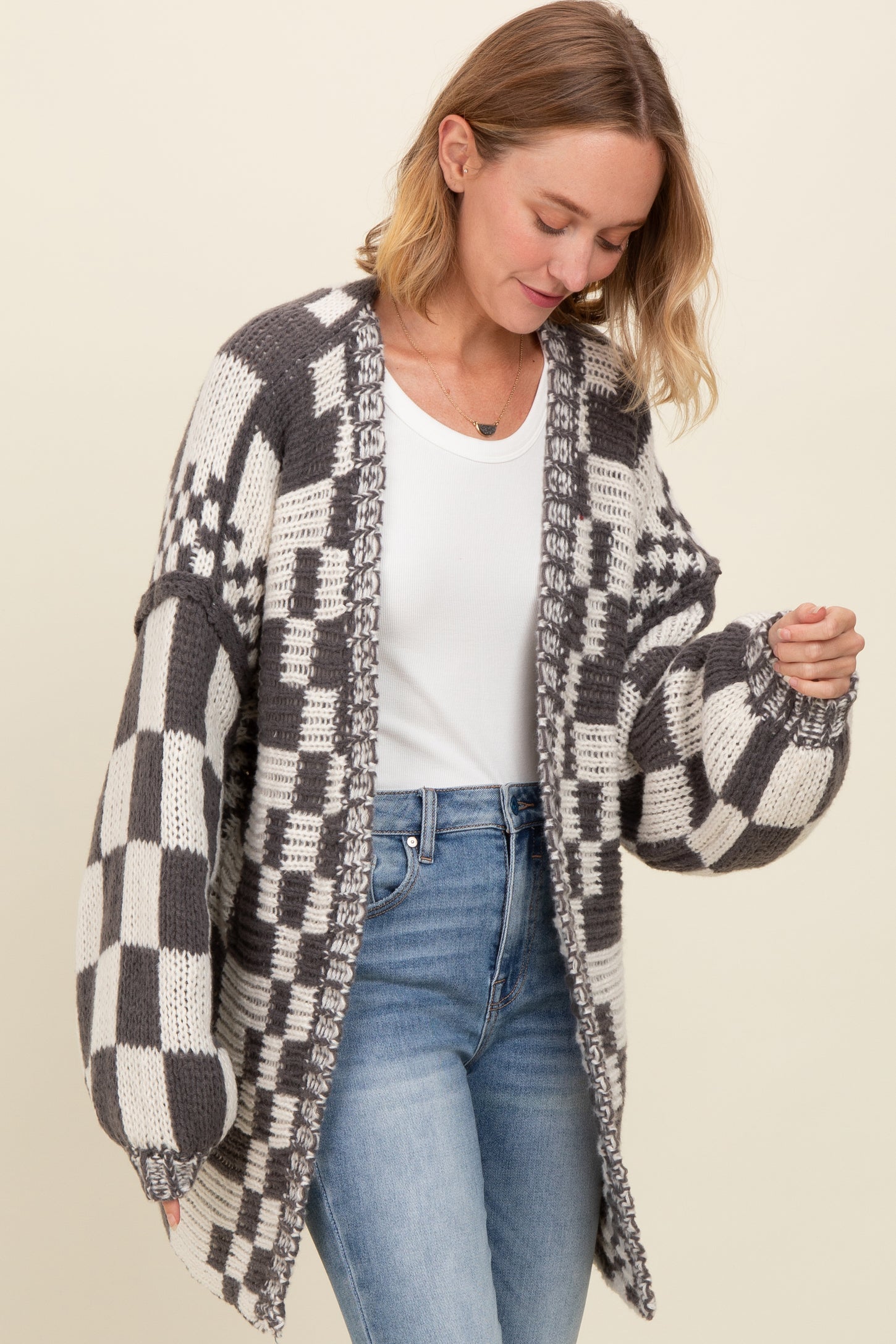 woman wearing a grey and white checkered oversized cardigan over a white top with blue jeans