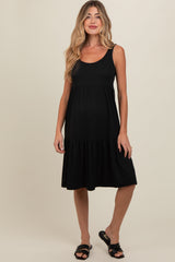 woman wearing a black ribbed maternity dress with a tiered skirt and a relaxed fit, holding her baby bump