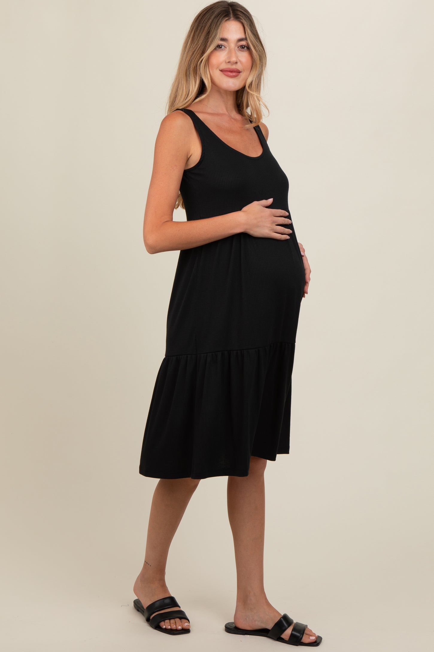 woman wearing a black maternity dress with a ribbed texture and a tiered skirt, cradling her baby bump