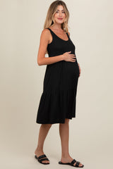 woman wearing a black maternity dress with a ribbed texture and a tiered skirt, cradling her baby bump