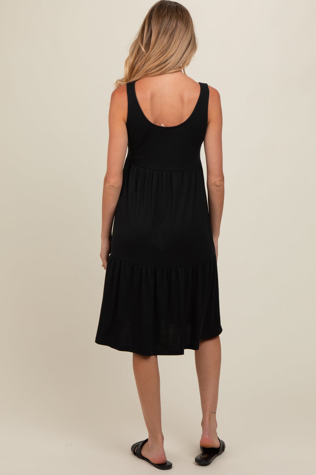 woman wearing a black sleeveless maternity dress with a tiered skirt and a relaxed fit, showing her back