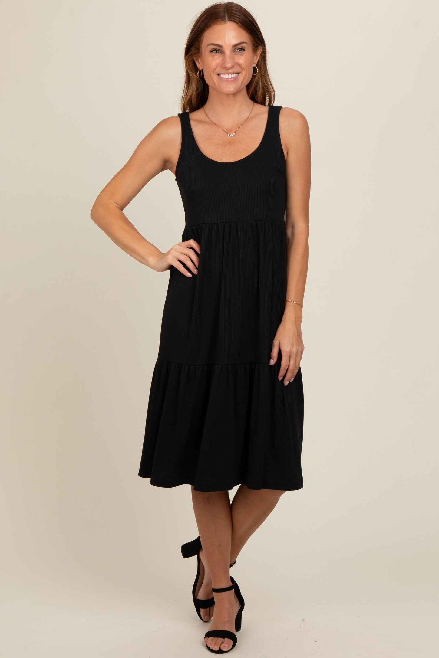woman wearing a black sleeveless tiered midi dress with a scoop neckline and black heels