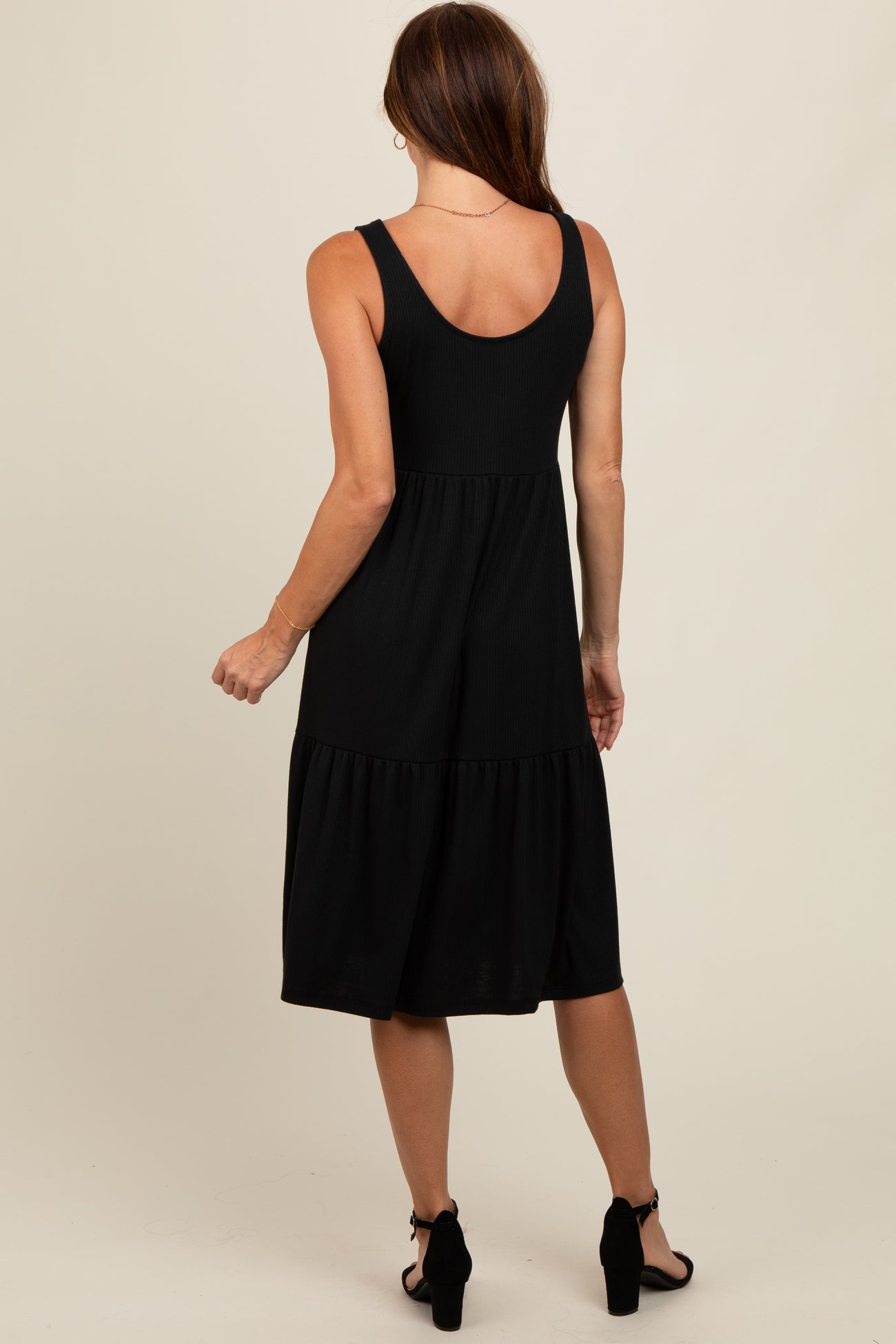 woman wearing a black ribbed midi dress with a tiered design, shown from the back