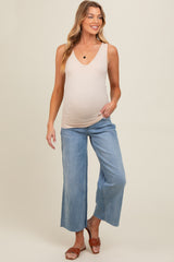 woman wearing a nude maternity tank top and light blue wide-leg jeans, showing her baby bump