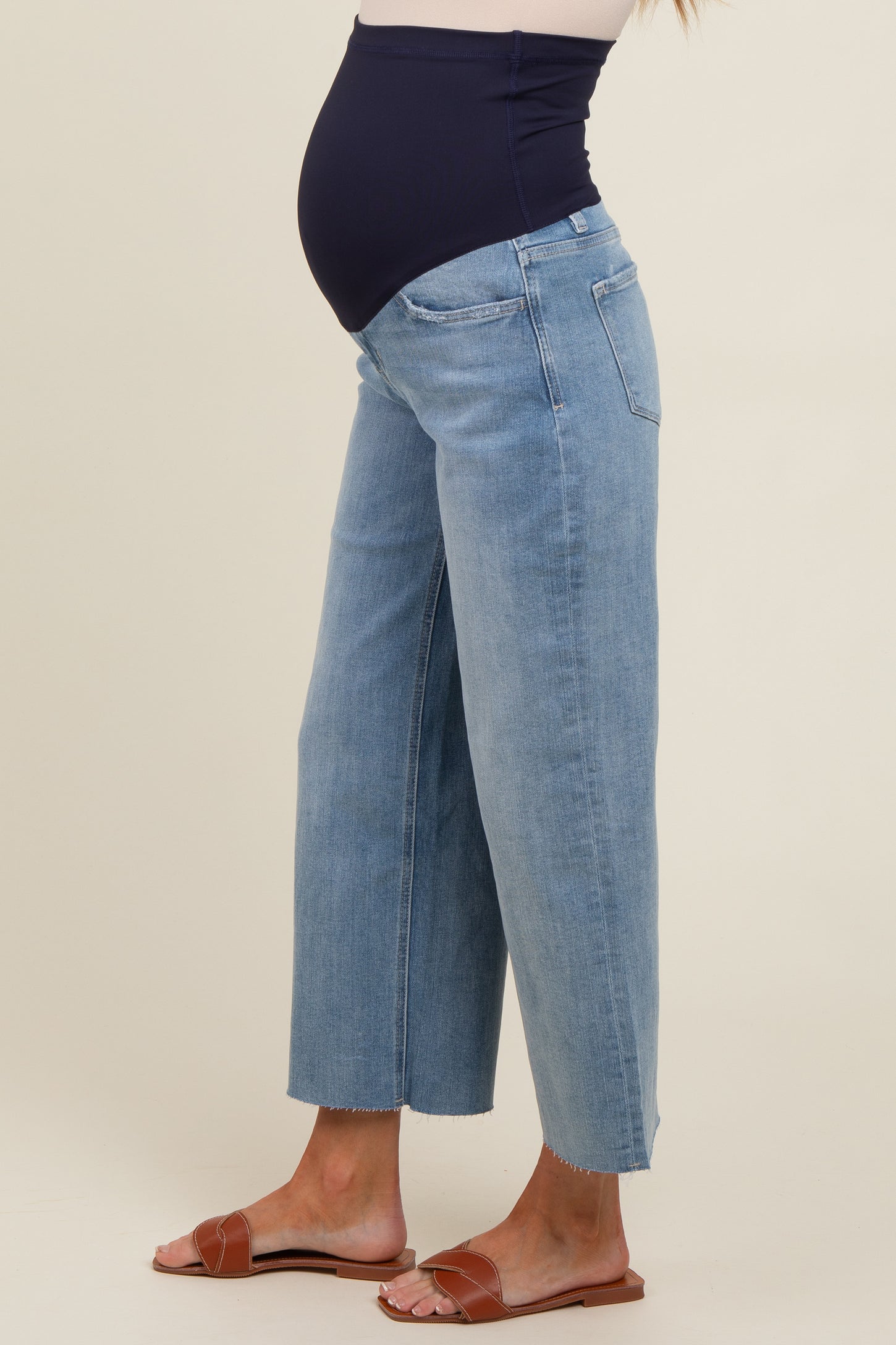 woman wearing light blue maternity jeans with a navy waistband and a visible baby bump, styled with brown sandals