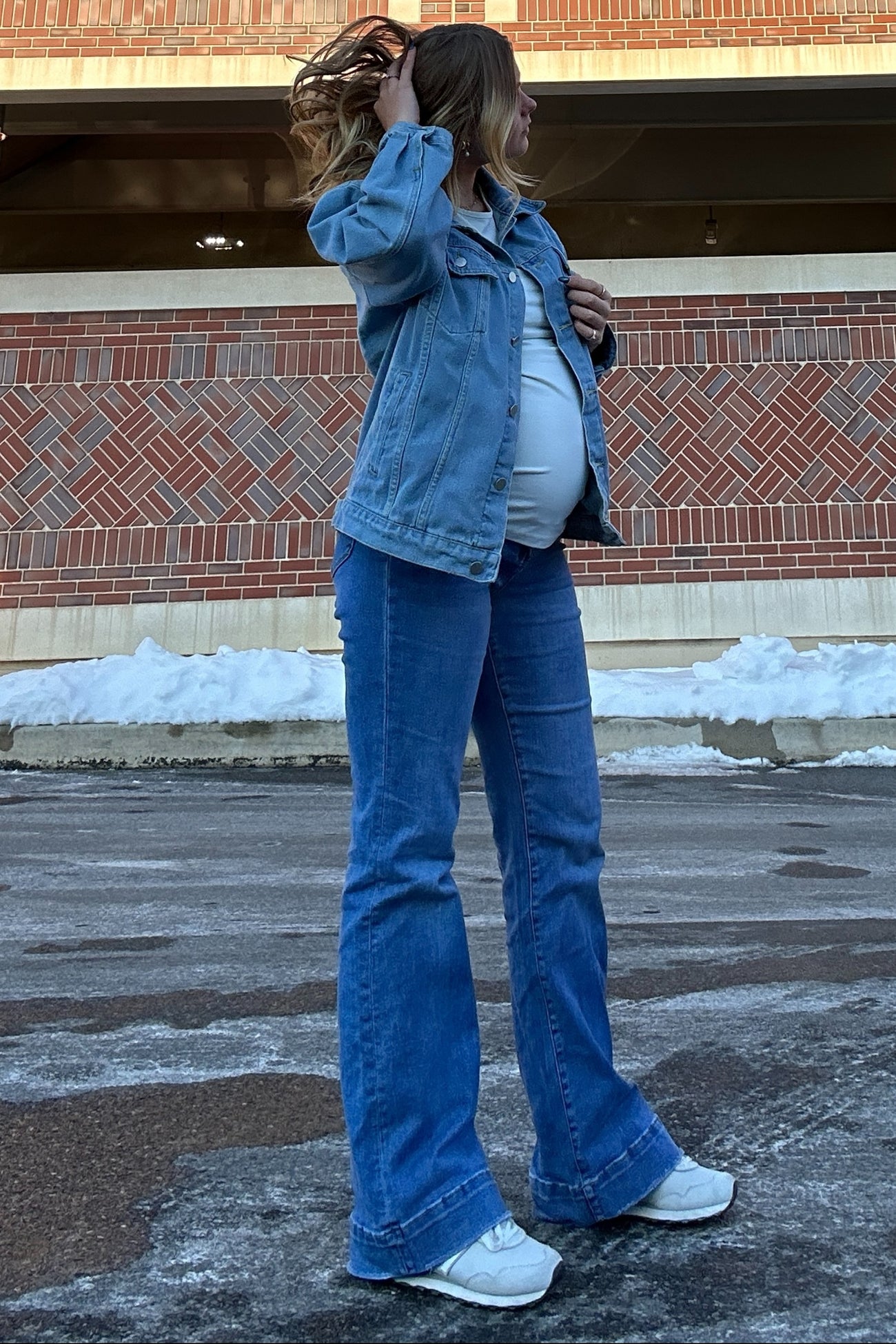 woman wearing a light blue denim jacket and flared jeans showcasing her baby bump in a winter setting