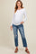 woman wearing a white long sleeve maternity top and distressed blue jeans, showing her baby bump