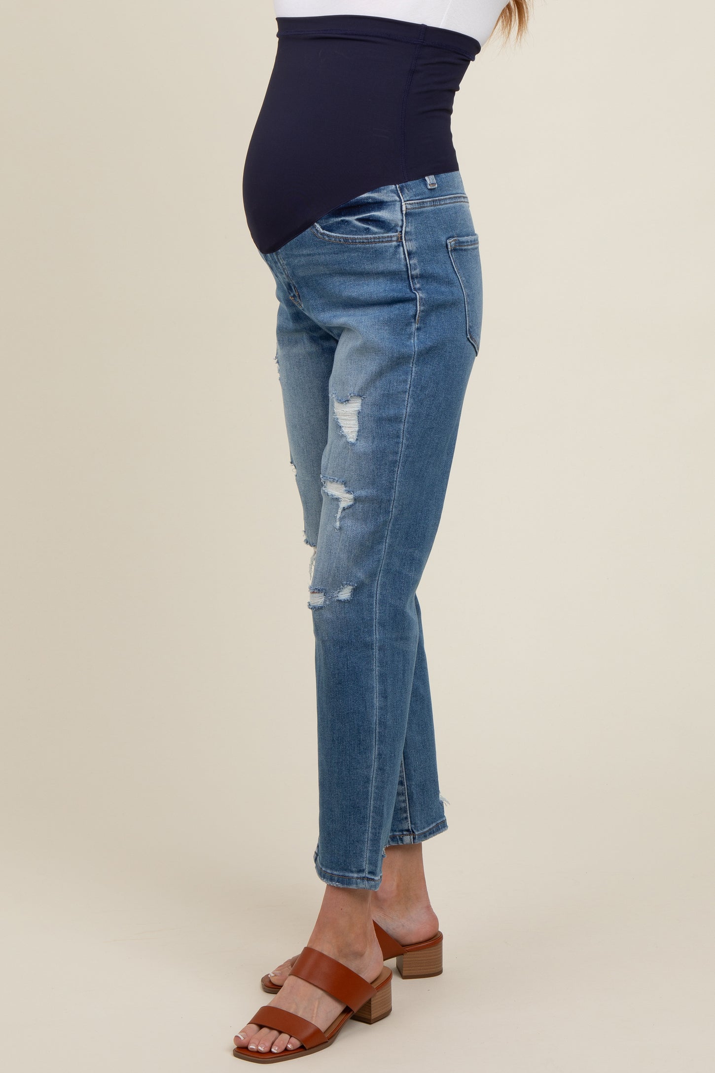 woman wearing distressed light blue maternity jeans with a dark blue over-the-bump waistband and brown block-heeled sandals