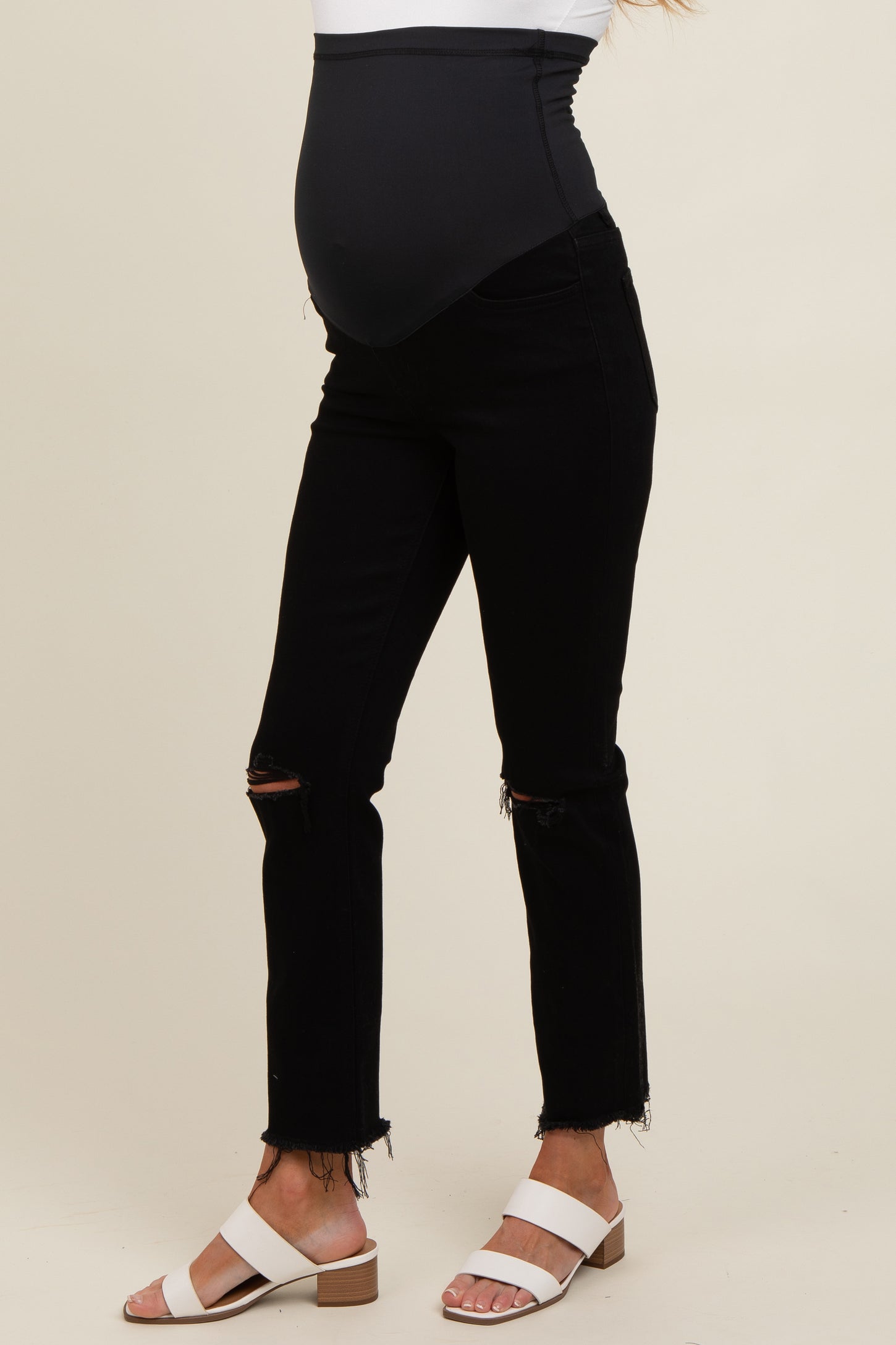 woman wearing black maternity jeans with a distressed hem and a stretchy belly panel, showing her baby bump