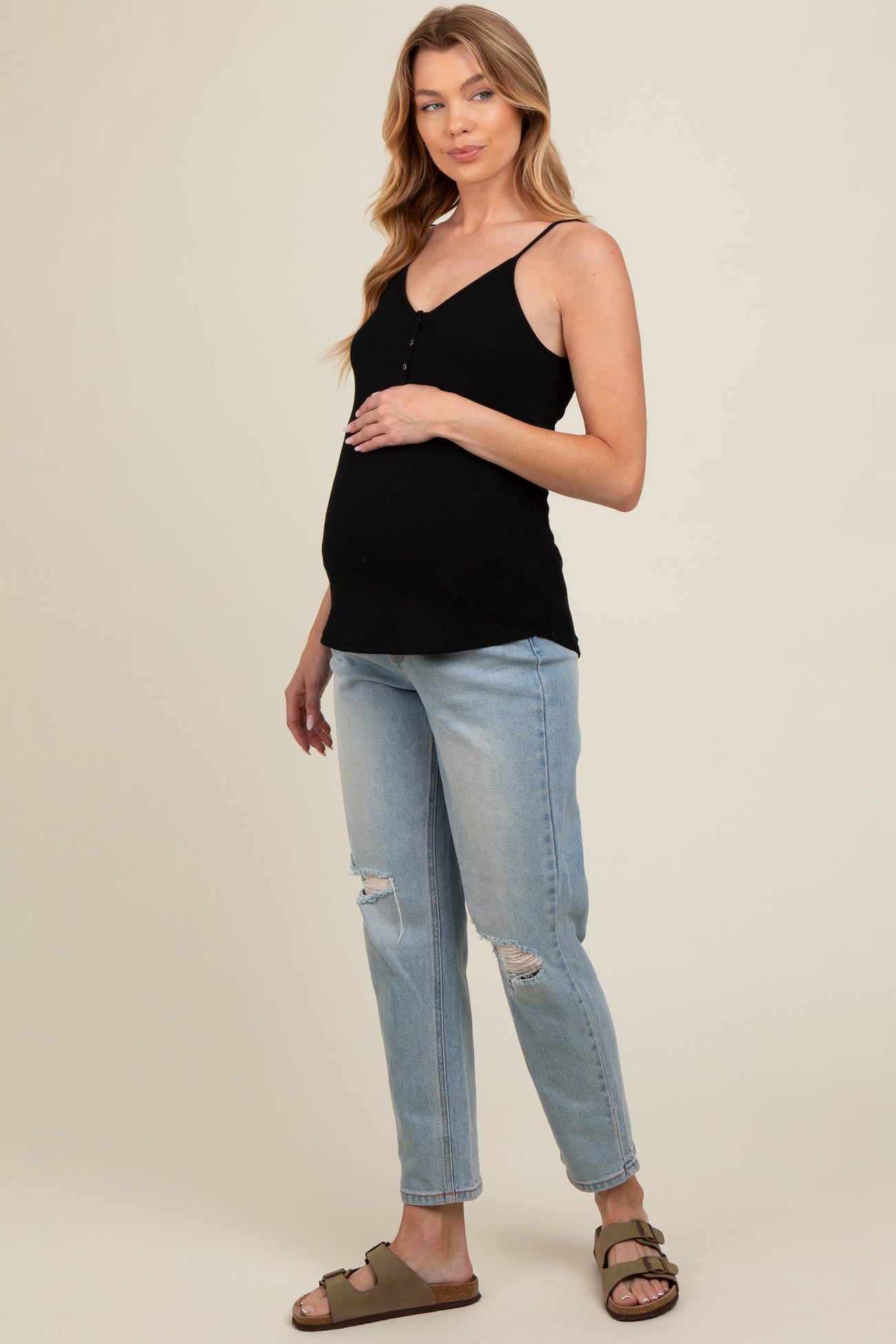 woman wearing a black maternity tank top and blue distressed jeans, showing her baby bump