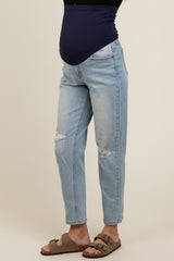 woman wearing light blue distressed maternity jeans with a dark blue support band and sandals, showing a baby bump