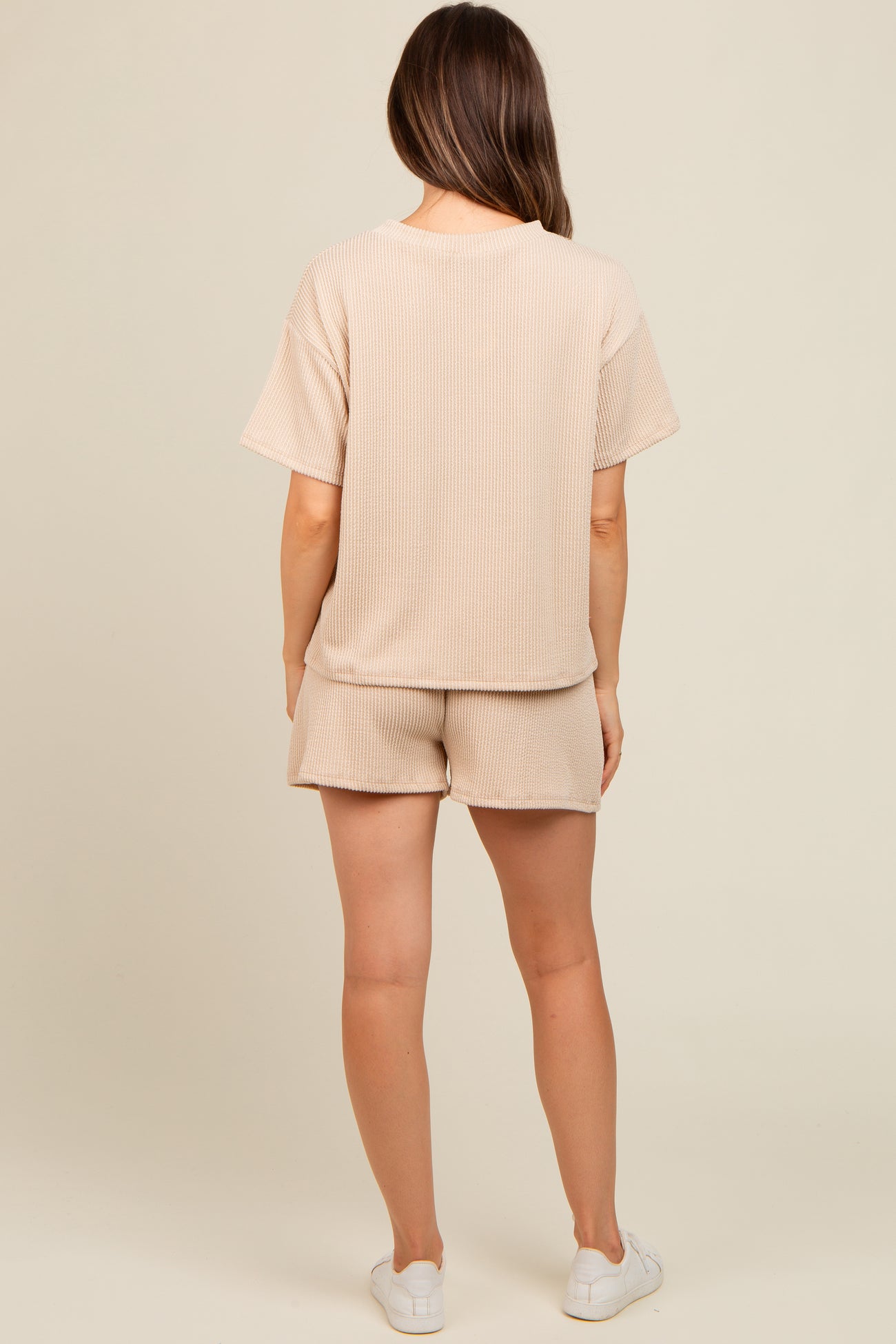 woman wearing a beige ribbed maternity loungewear set featuring a short sleeve top and matching shorts