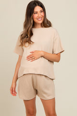 woman wearing a beige ribbed maternity top and matching shorts, holding her baby bump