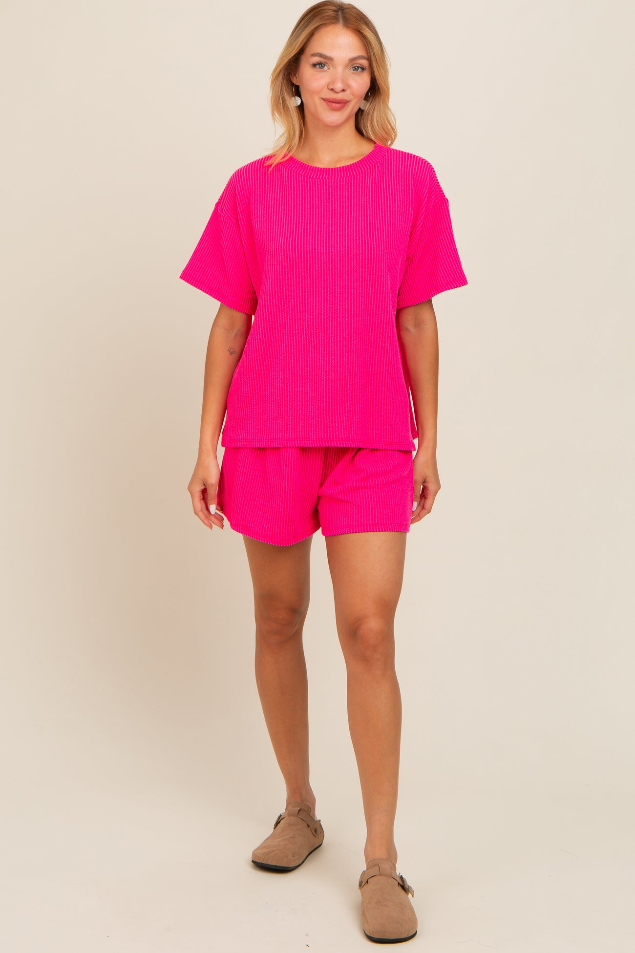 woman wearing a bright pink ribbed short-sleeve top and matching shorts, standing against a neutral background