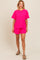 woman wearing a bright pink ribbed short-sleeve top and matching shorts, standing against a neutral background