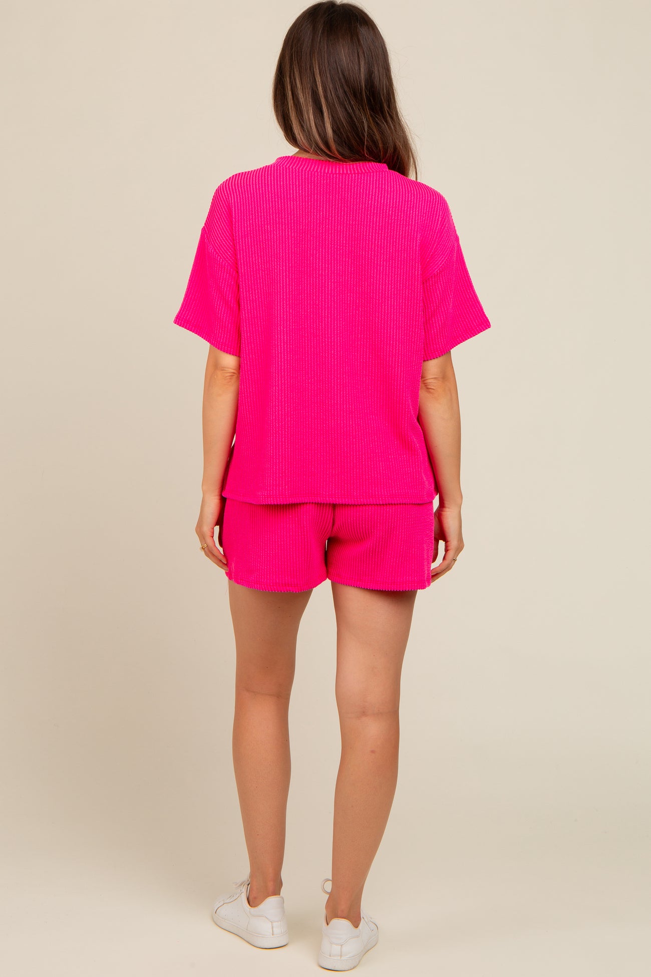 woman wearing a bright pink maternity short set, showing a relaxed fit top and shorts from the back