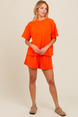 woman wearing an orange ribbed short sleeve top and matching shorts, standing with hands in front