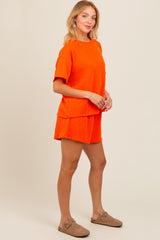 woman wearing an orange ribbed short sleeve top and matching shorts, styled with tan slip-on shoes