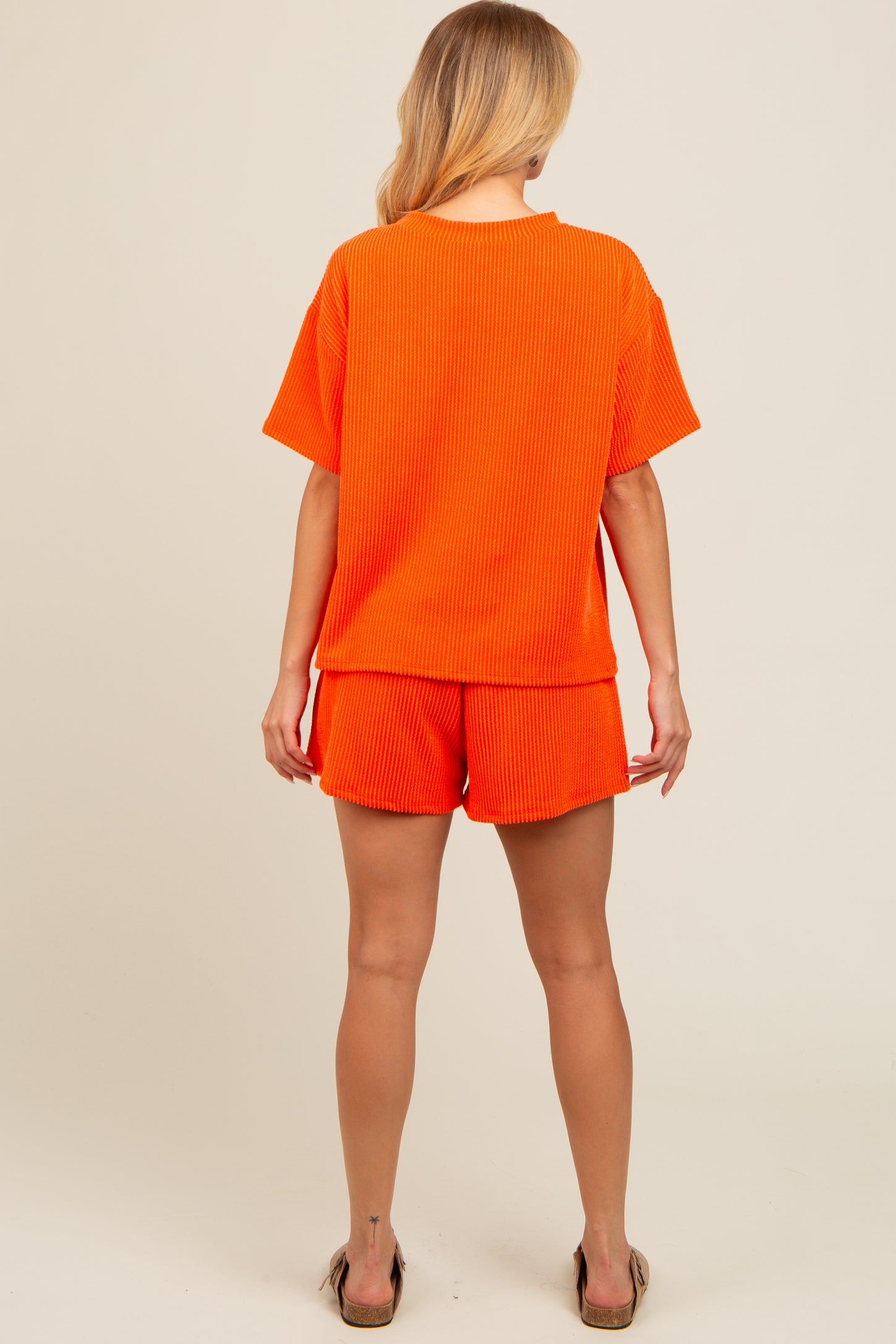 woman wearing an orange ribbed short sleeve top and matching shorts, viewed from the back