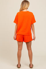 woman wearing an orange ribbed short sleeve top and matching shorts, viewed from the back