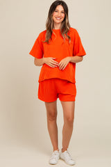 woman wearing an orange ribbed maternity top and matching shorts, holding her baby bump