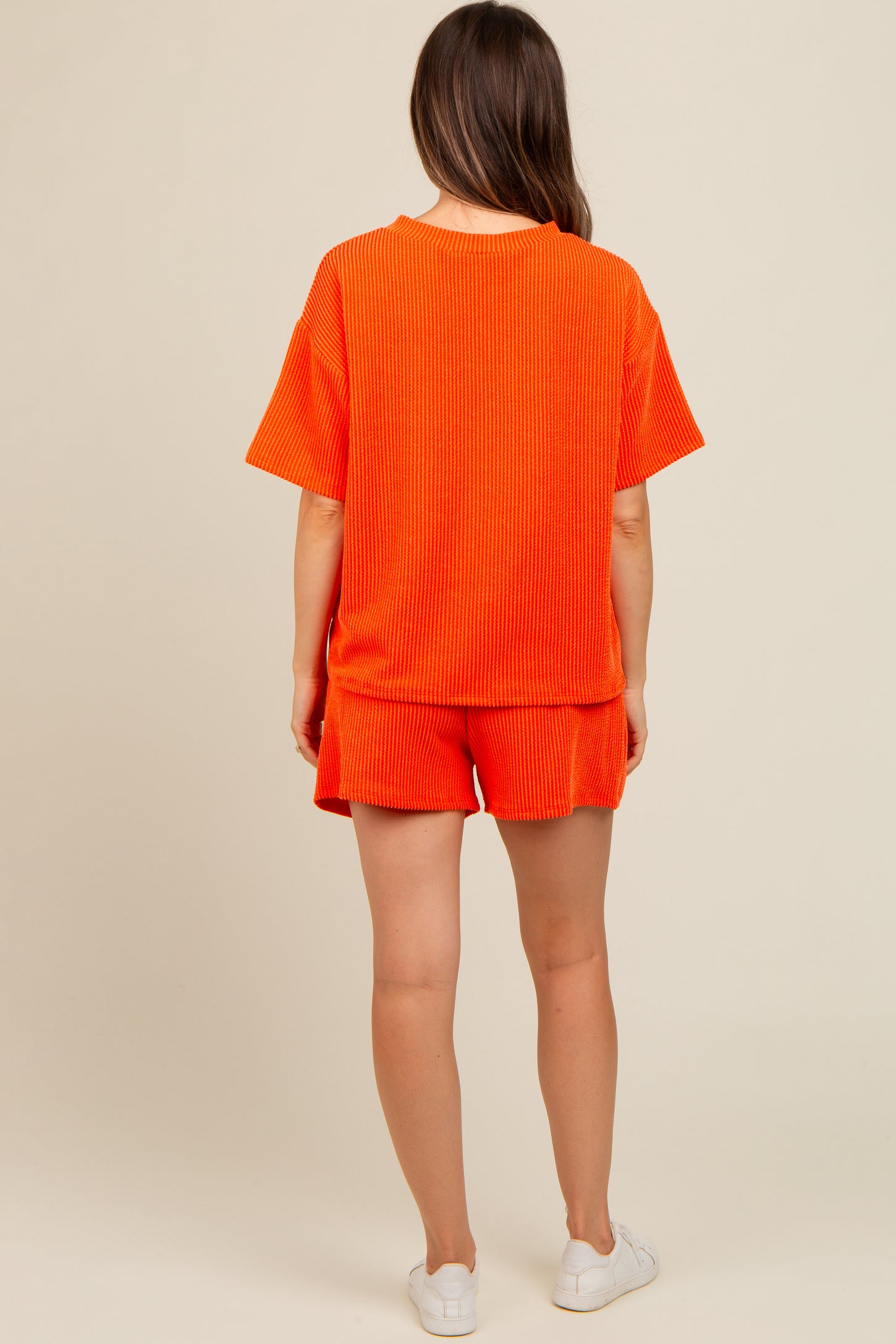 woman wearing an orange ribbed maternity short set, showing the back view with a relaxed fit and short sleeves