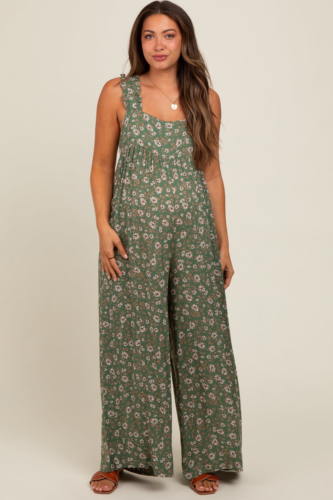 woman wearing a green floral maternity jumpsuit with wide legs and adjustable straps, showcasing her baby bump