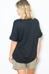 woman wearing a black oversized t-shirt with rolled sleeves and beige shorts, viewed from the back