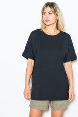 woman wearing a black oversized t-shirt and beige shorts standing against a white backdrop
