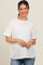 woman wearing a white short sleeve maternity top and smiling, with a baby bump visible, styled with a necklace
