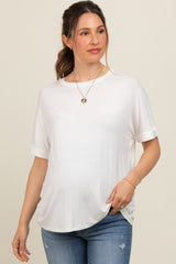 woman wearing a white maternity top with rolled short sleeves and a visible baby bump, styled with jeans