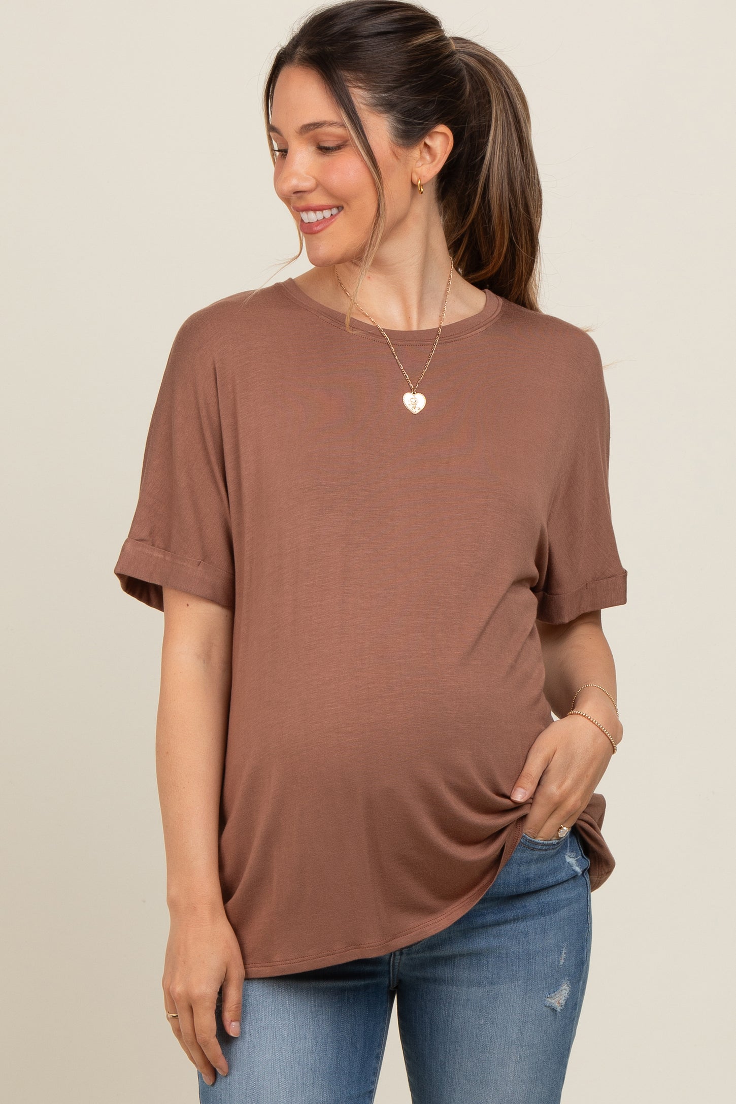 woman wearing a brown short sleeve maternity top and holding her baby bump with a smile