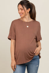 woman wearing a brown short sleeve maternity top and holding her baby bump with a smile