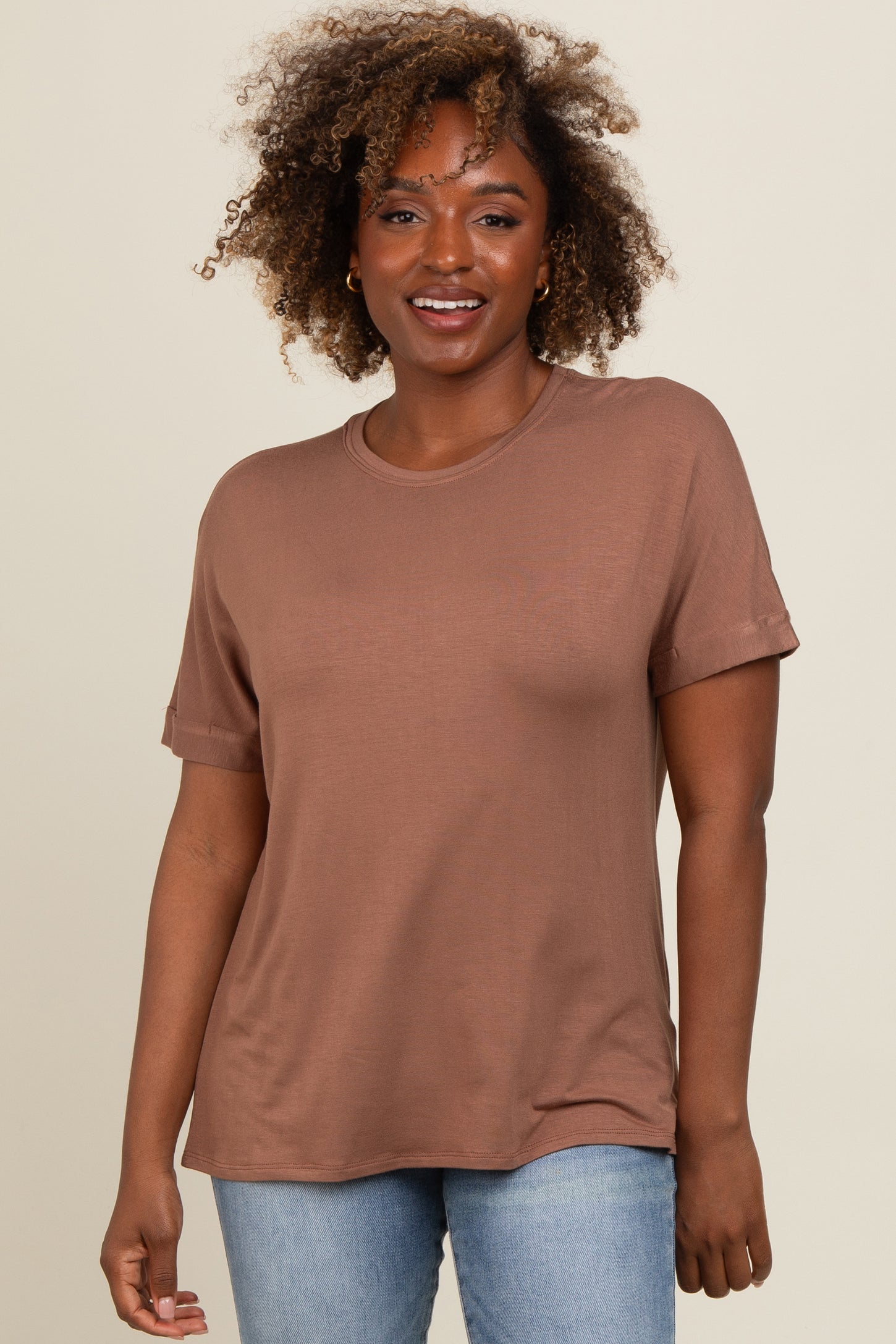 woman wearing a brown short sleeve t-shirt with rolled cuffs and relaxed fit, smiling at the camera