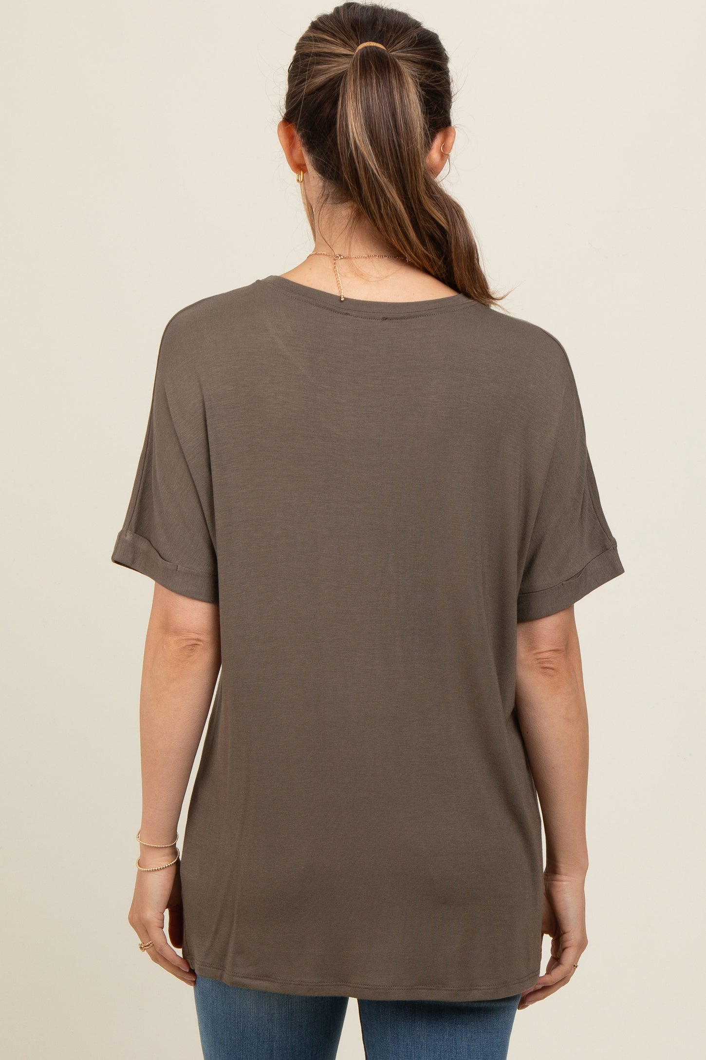 woman wearing a loose-fitting olive green maternity top, viewed from the back, with rolled sleeves and a relaxed silhouette