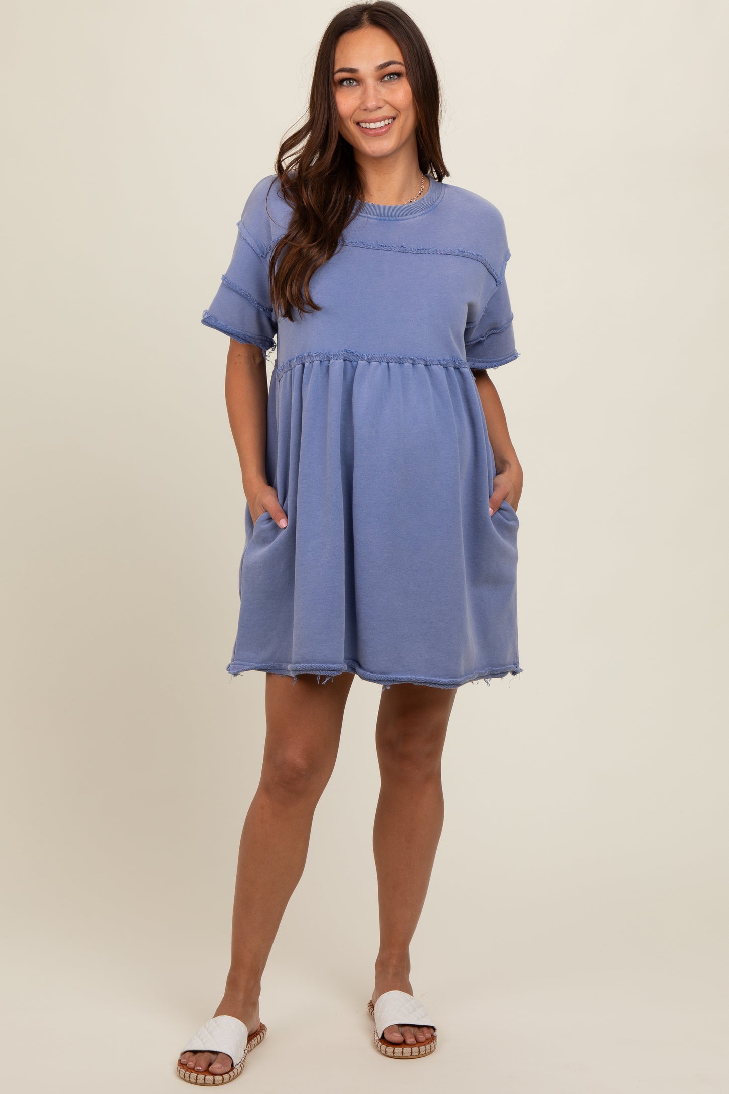 woman wearing a dusty blue short sleeve maternity dress with pockets and frayed hem, showing her baby bump
