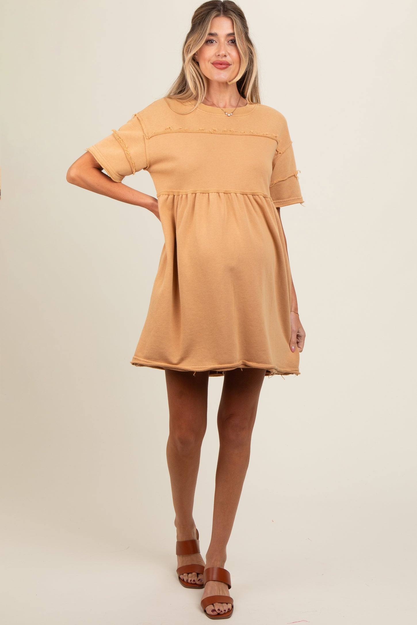 woman wearing a tan short sleeve maternity dress with a flared skirt and visible baby bump