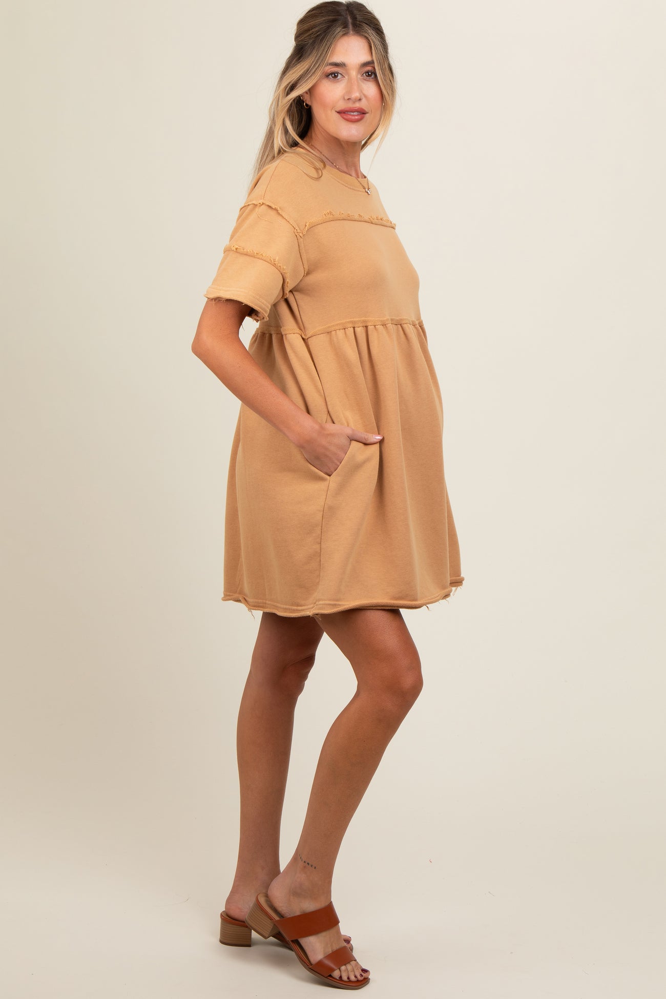 woman wearing a tan maternity dress with short sleeves and pockets, showing a baby bump