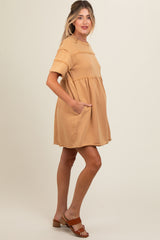 woman wearing a tan maternity dress with short sleeves and pockets, showing a baby bump