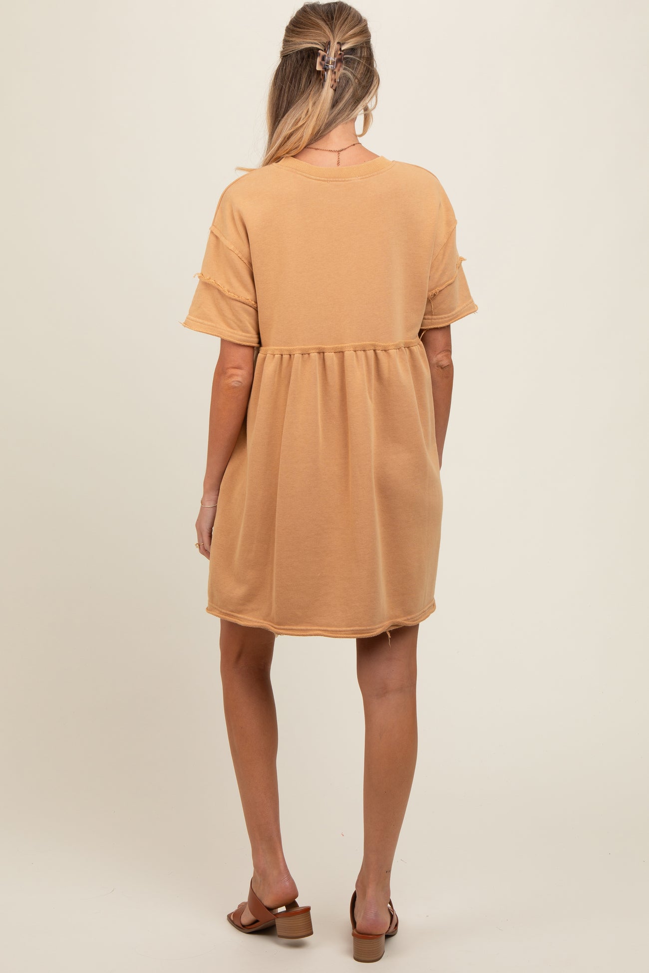 woman wearing a light brown short sleeve maternity dress with a loose fit and ruffled details, showing her baby bump