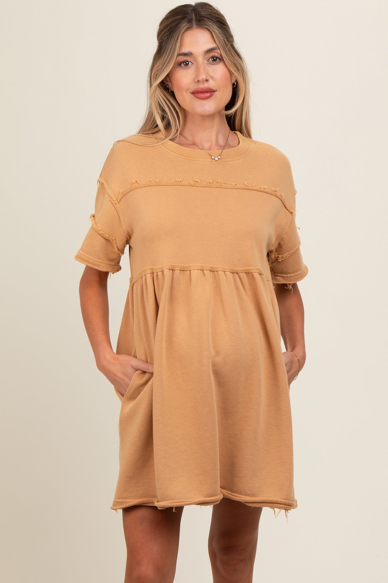 woman wearing a tan maternity dress with a tiered design and pockets, featuring distressed details and short sleeves