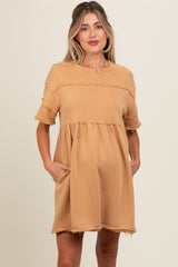 woman wearing a tan maternity dress with a tiered design and pockets, featuring distressed details and short sleeves
