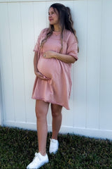 woman wearing a blush pink oversized maternity dress and gently cradling her baby bump
