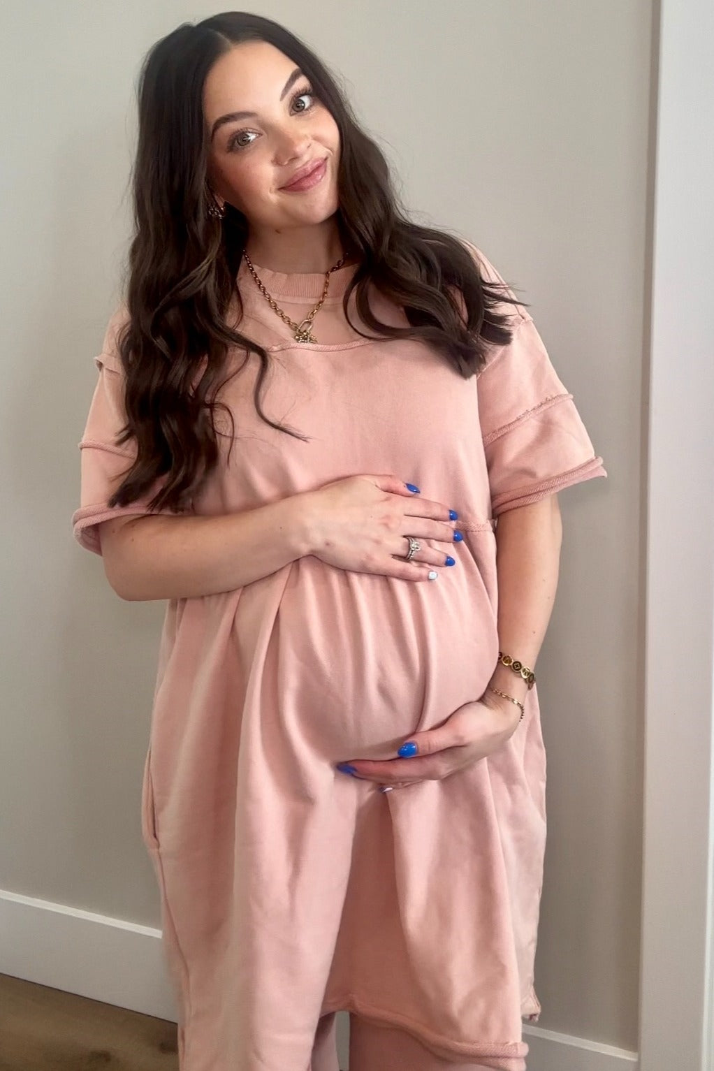 woman wearing a blush pink oversized maternity dress and holding her baby bump