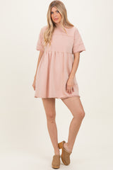 woman wearing a light pink oversized short sleeve dress with a tiered design and raw hem details