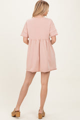 woman wearing a light pink short-sleeve dress with a gathered waist, showing the back view and paired with tan clogs
