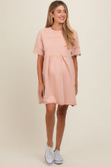 woman wearing a blush pink short sleeve maternity dress with a relaxed fit and distressed hem